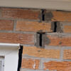 A brick wall displaying stair-step cracks and messy tuckpointing on a Dartmouth home
